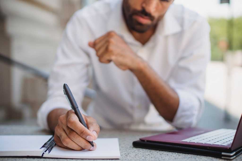 man writes on notepad while resting on elbow