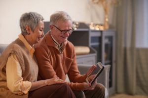 older couple sits on sofa smiling at tablet screen