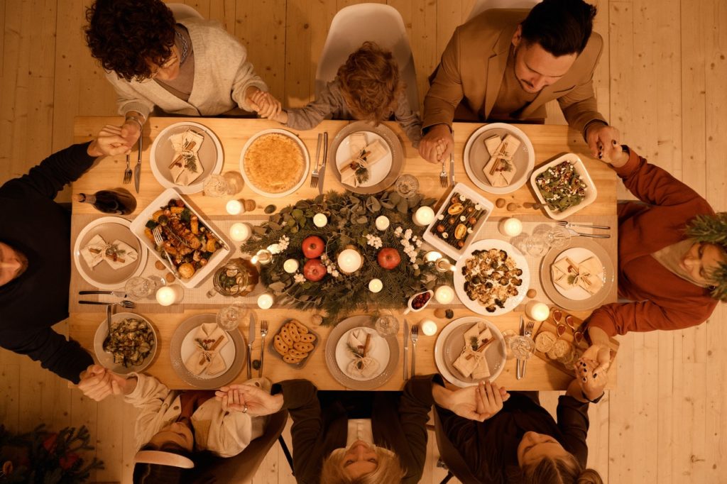 overhead shot of a holiday dinner table with family holding hands around it