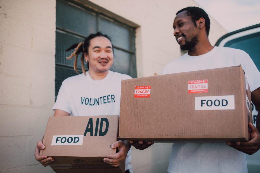 two men in volunteer shirts carry boxes of food donations