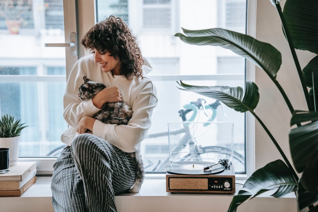 woman sits near window and cuddles cat on her lap