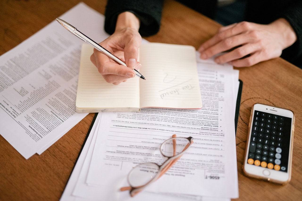 woman's hands take notes on top of tax documents and calculator spread over tabletop