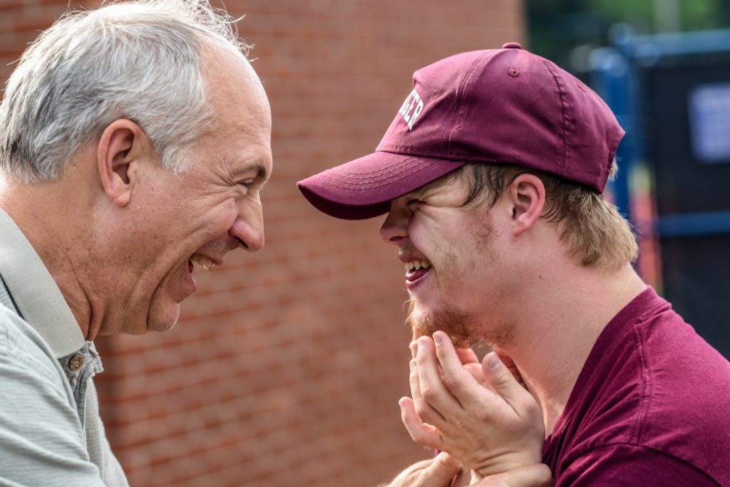 old man and young man with downs syndrome smile at each other