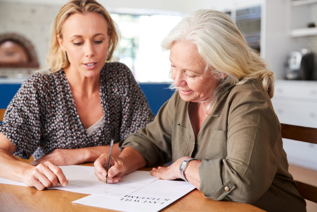 older woman signs her last will and testament with her daughter